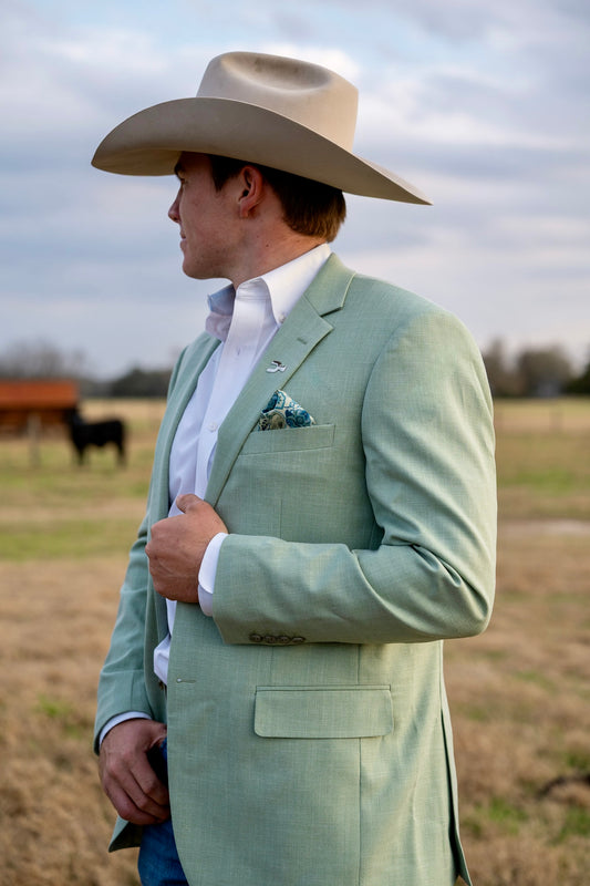 Man wearing a light green suit and cowboy hat in an outdoor setting with a horse in the background. The Cowboy Sport Coat Company Featuring the Mint Julip Blazer
