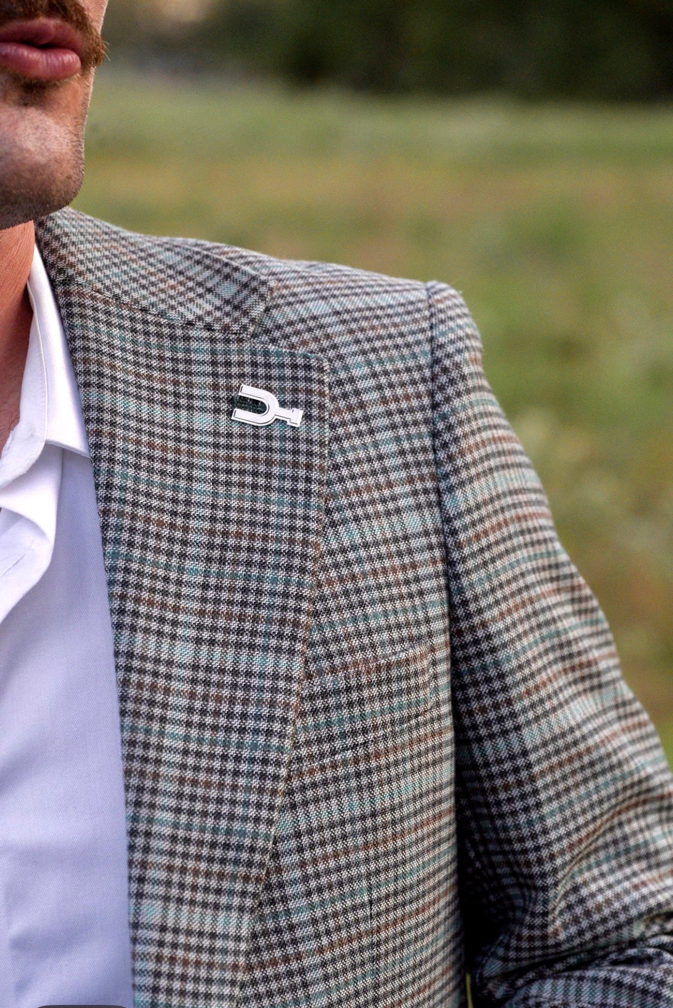 Person wearing a checkered blazer with a distinctive lapel pin in an outdoor setting
