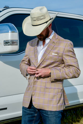 Man wearing a beige checkered blazer and cowboy hat standing next to a white truck.
