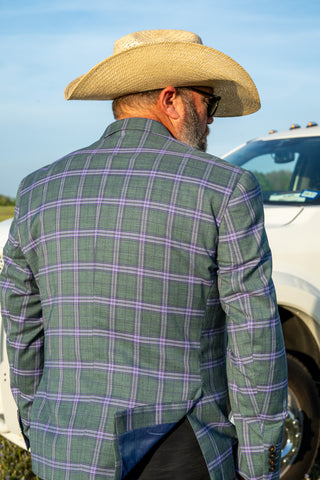 Man wearing a green checkered jacket and cowboy hat standing next to a white truck.