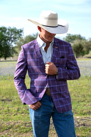 Man wearing a purple plaid blazer, white shirt, and cowboy hat in an outdoor setting.