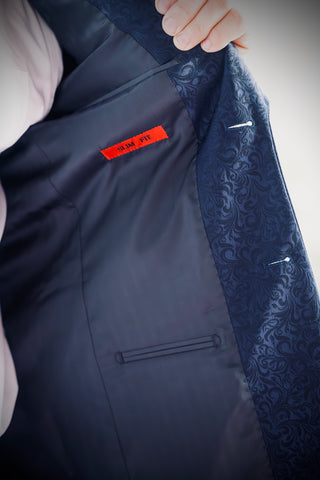 Close-up of a dark navy suit jacket interior with a hand holding the lapel, showing a patterned navy lining and a small red interior label.