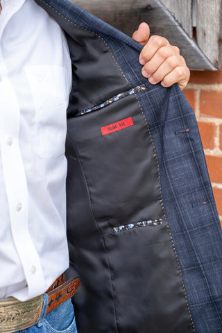 Close-up of a person wearing a dark blue plaid blazer, holding the lapel open to show the black interior lining and a small red brand label that reads 'SILK ST'.
