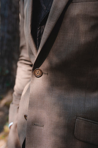 Close-up of a brown suit jacket with a button and pocket detail.